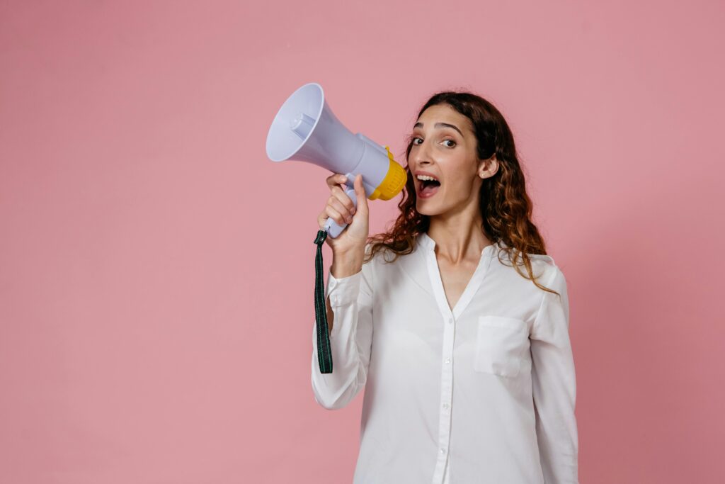 pexels photo 8638300 8638300 Woman in white shirt holding megaphone against a pink background, confidently speaking.